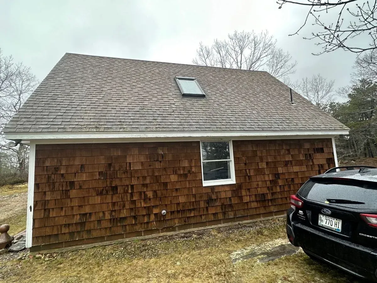A car is parked in front of a house with a roof that has a skylight.