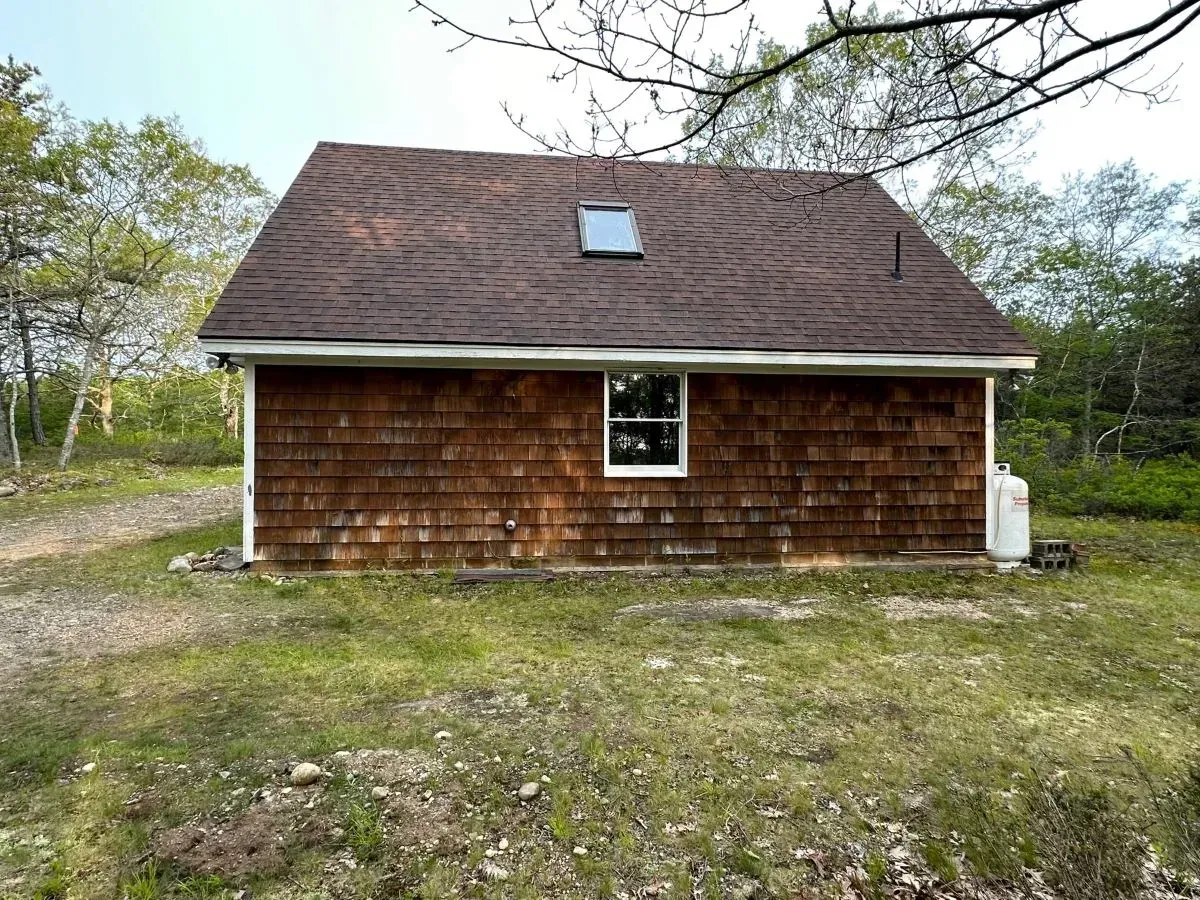 A small house with a brown roof is sitting in the middle of a grassy field.