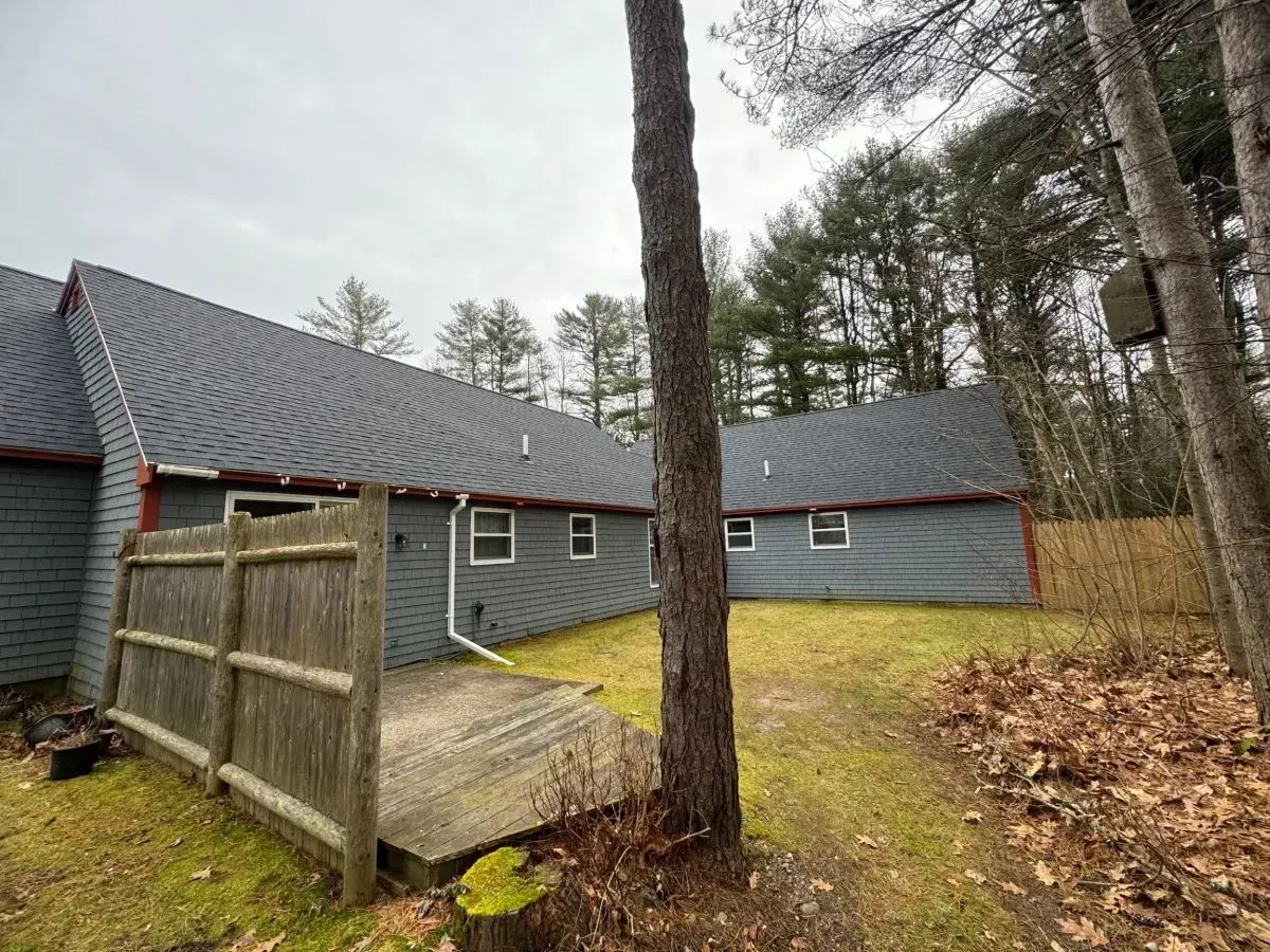 The backyard of a house with a wooden fence and a deck surrounded by trees.