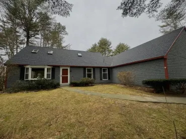 A gray house with a black roof and a red door.