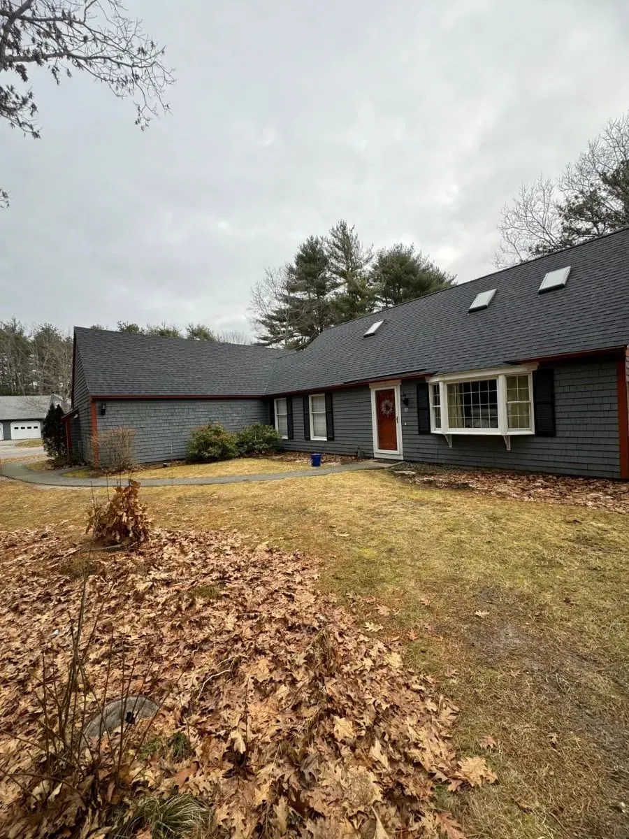 A large house with a black roof and a lot of leaves on the ground.