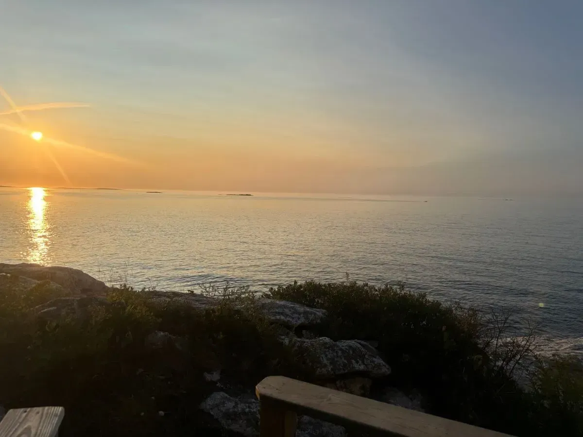 The sun is setting over the ocean with a boat in the distance.