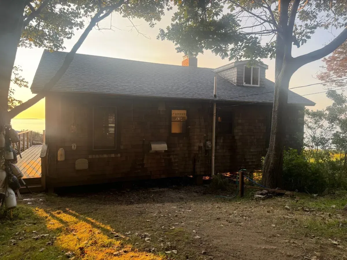 A small wooden house is sitting in the middle of a field surrounded by trees.