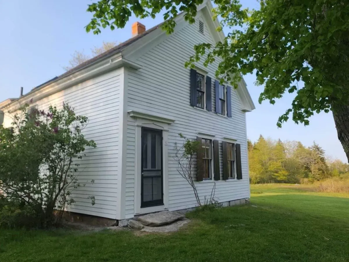 A white house with black shutters is sitting in the middle of a grassy field.