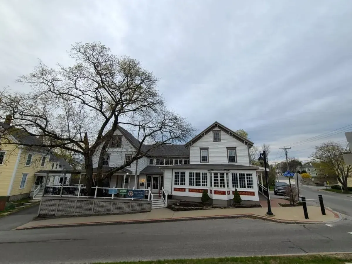 A large white house is sitting on the corner of a street next to a tree.