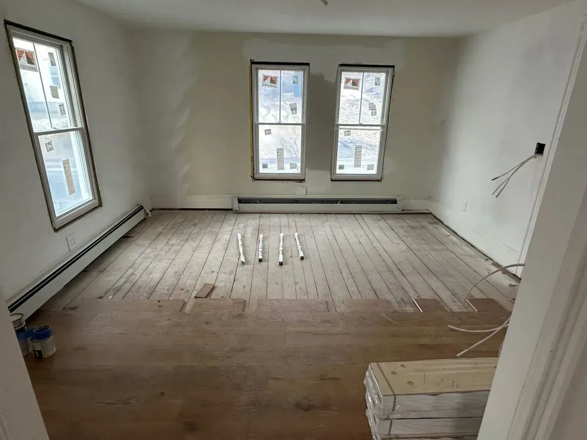 An empty room with a wooden floor and two windows.