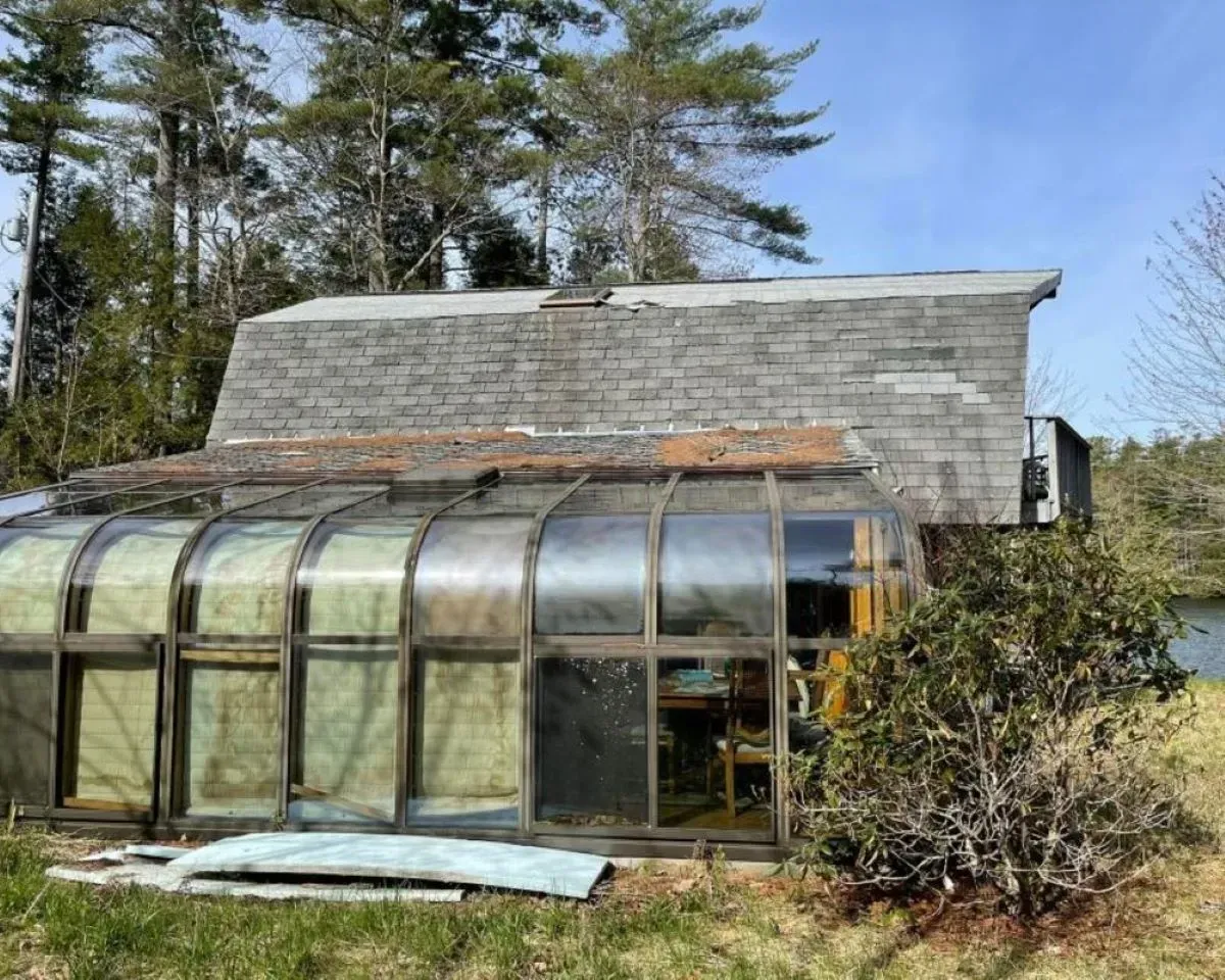 A greenhouse is sitting in the middle of a field next to a house.