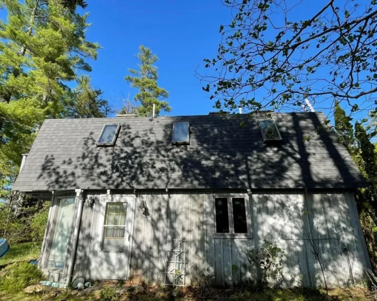 A white house with a gray roof is surrounded by trees