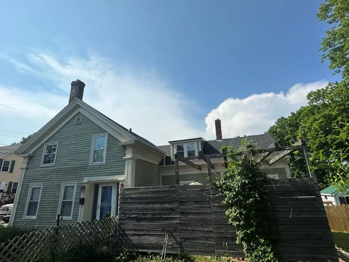 A house with a wooden fence in front of it and a blue sky in the background.