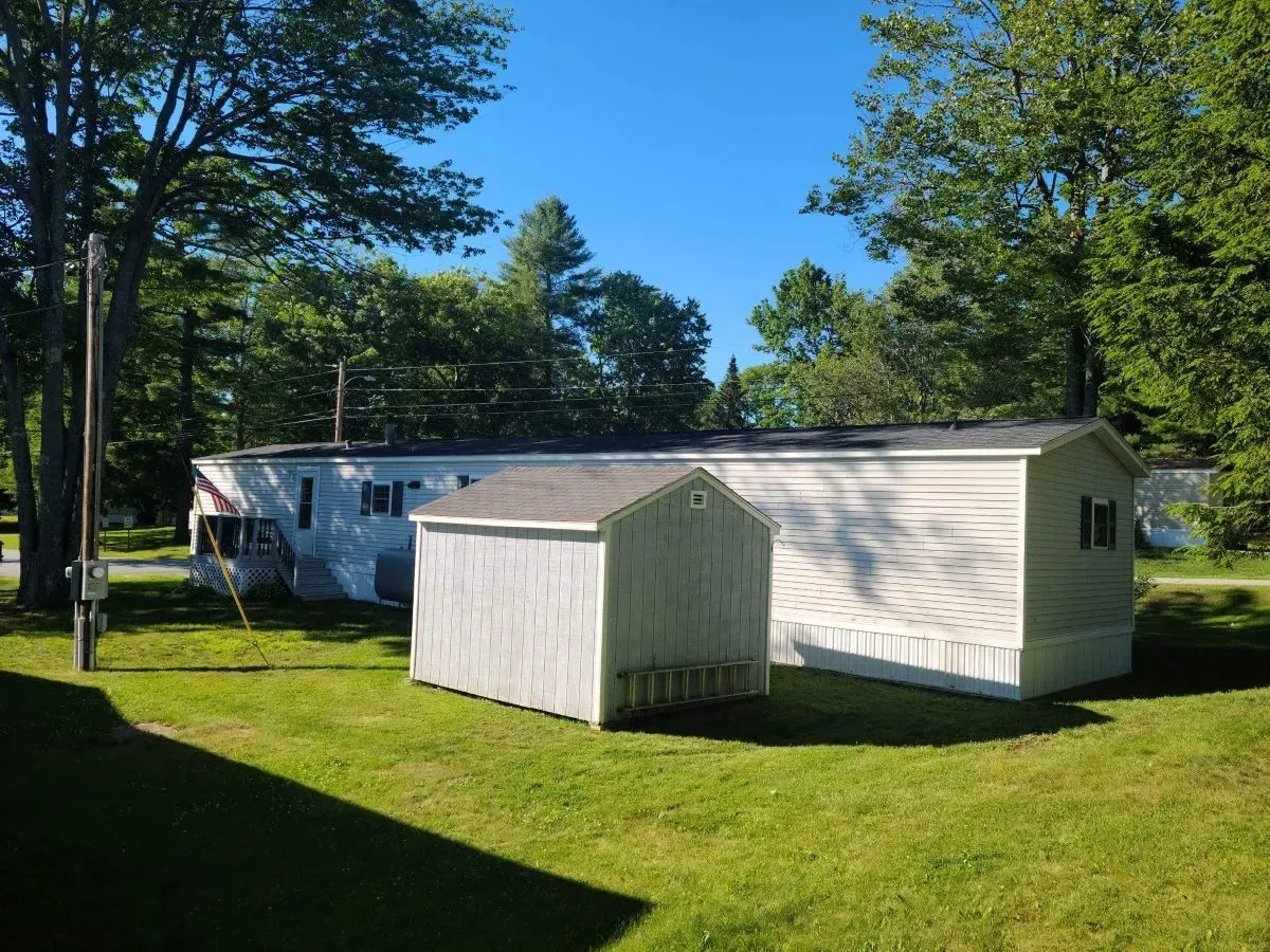 A white shed is sitting in the grass next to a mobile home.