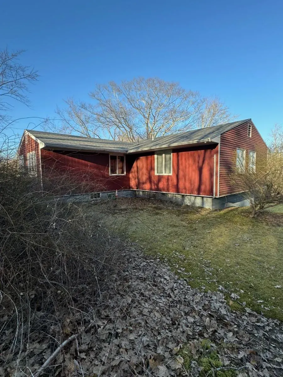 A red house is sitting in the middle of a grassy field.