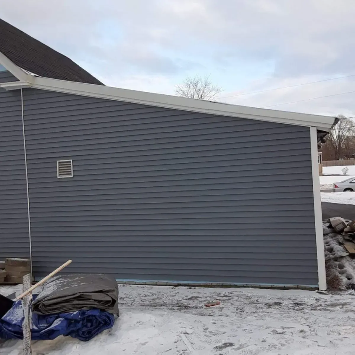 A gray house with a white roof is sitting in the snow.