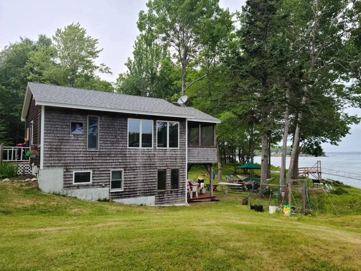 A large house is sitting on top of a lush green hill next to a body of water.