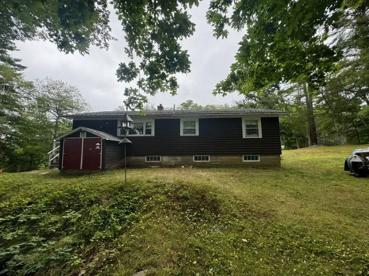 A house with a red shed in the backyard is surrounded by trees and grass.