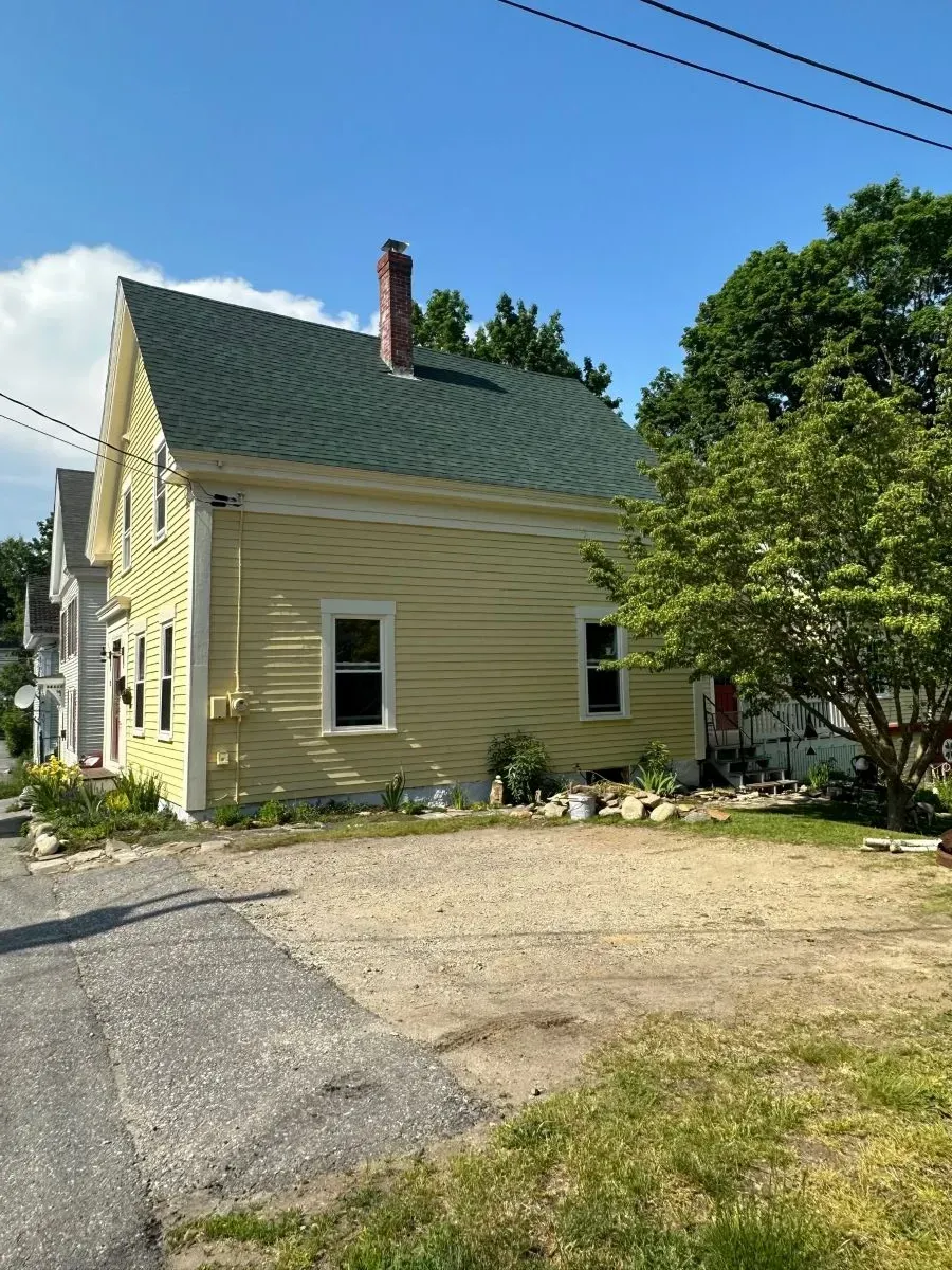 A yellow house with a green roof is sitting on the side of the road.