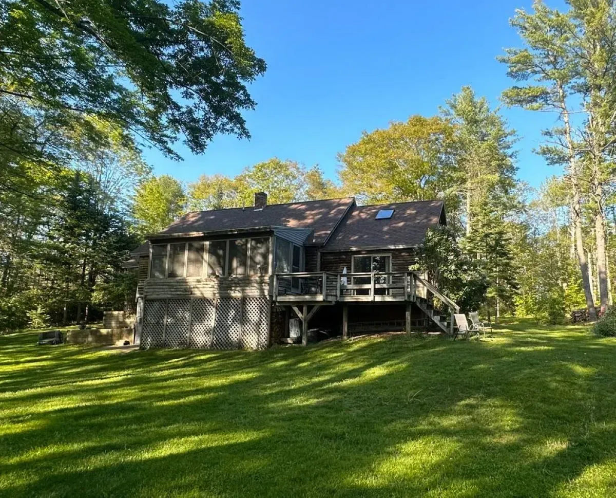 A house in the middle of a lush green field with trees in the background.