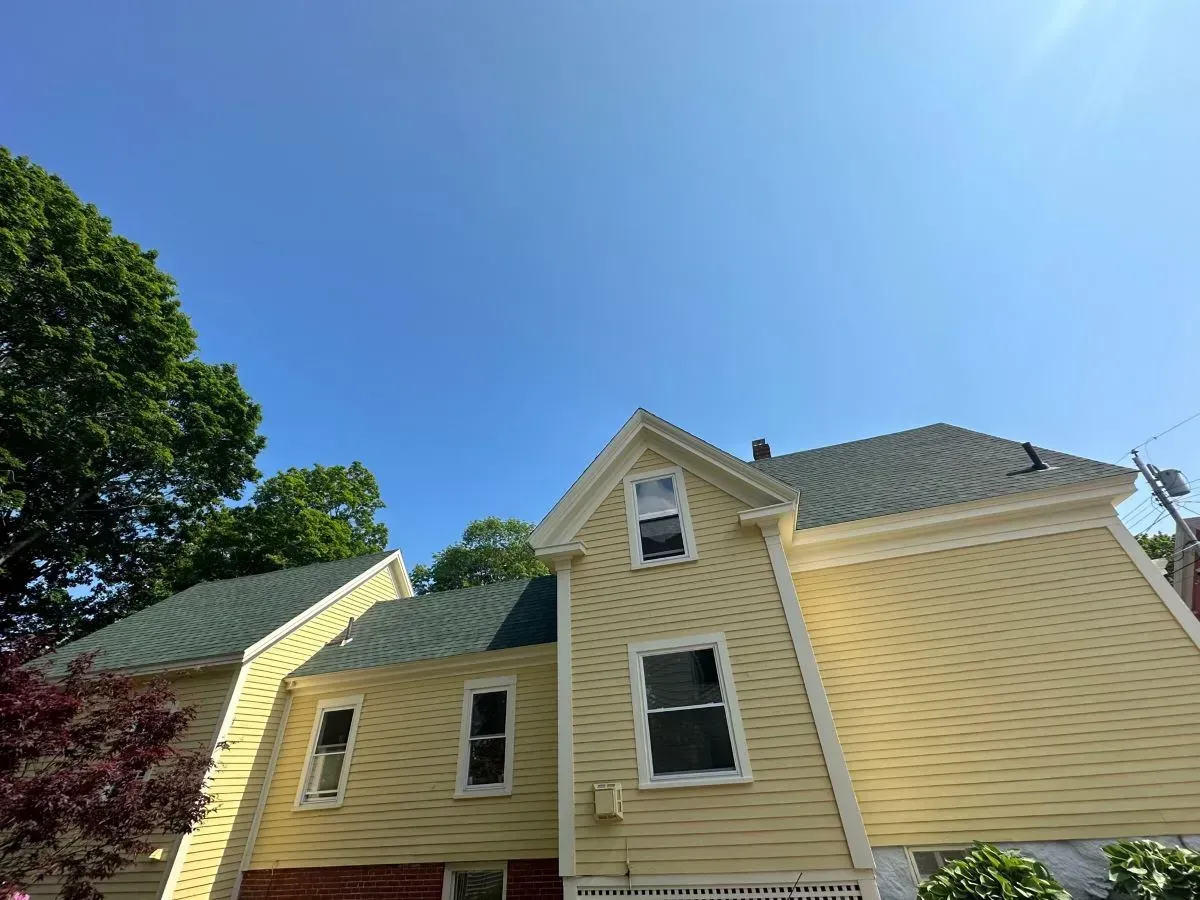 A yellow house with a green roof and a blue sky in the background.