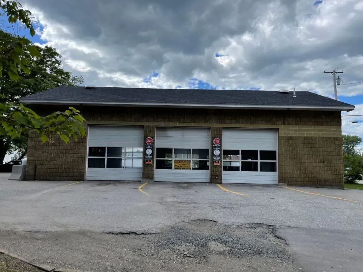 A brick building with two garage doors and a parking lot in front of it.