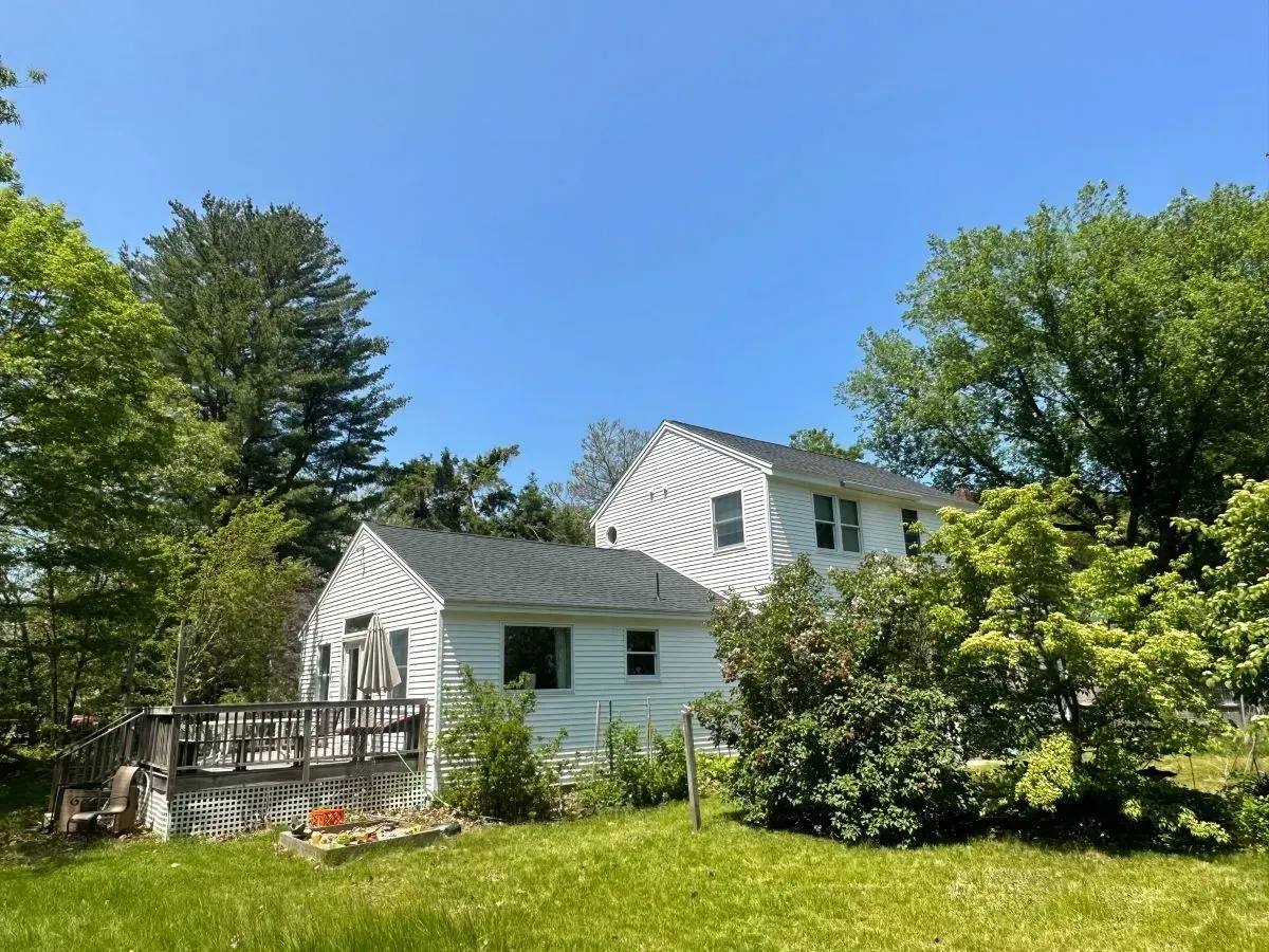 A white house with a black roof is surrounded by trees