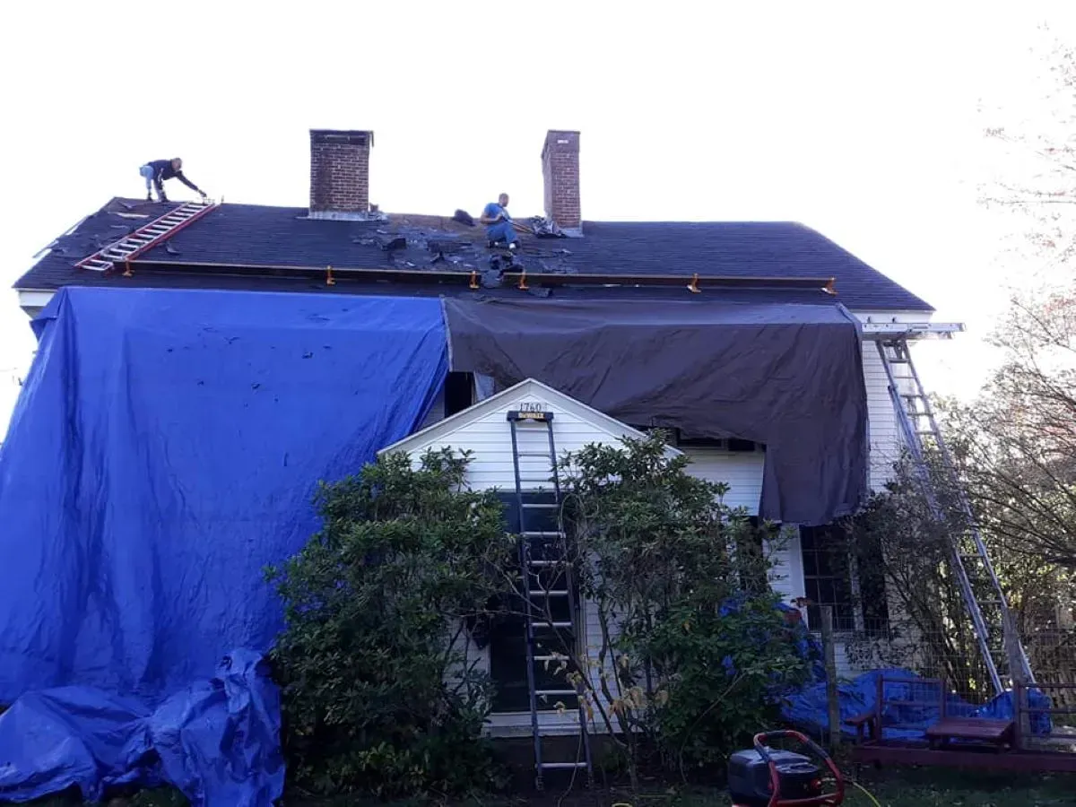 A house is covered in a blue tarp and workers are working on the roof