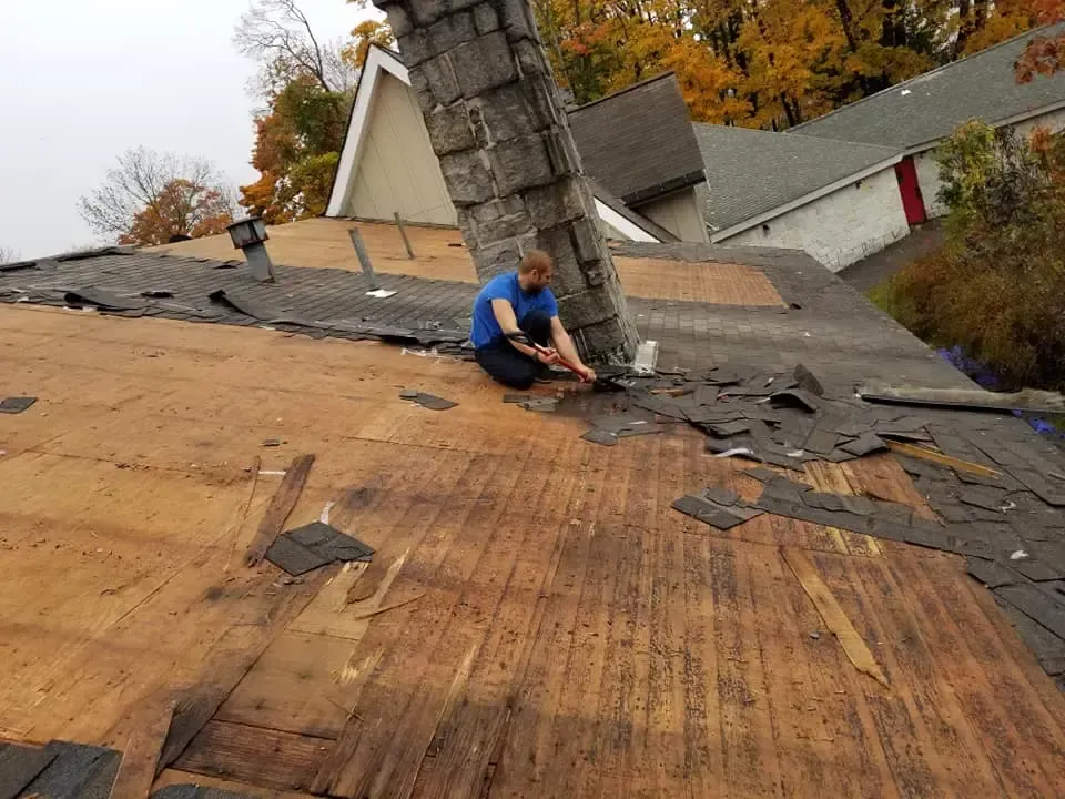 A man is kneeling on the roof of a house.