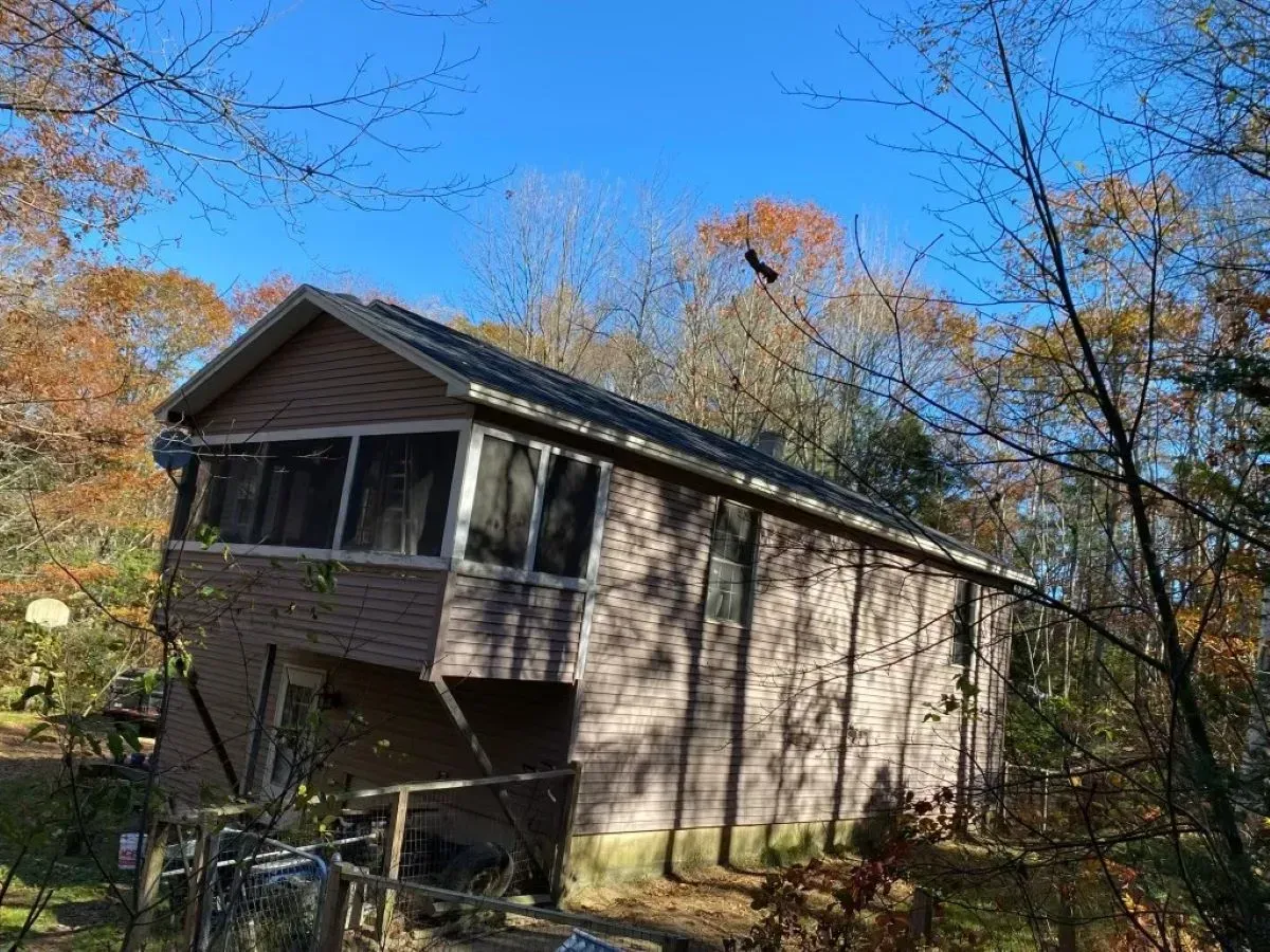 A small house with a screened in porch is surrounded by trees on a sunny day.