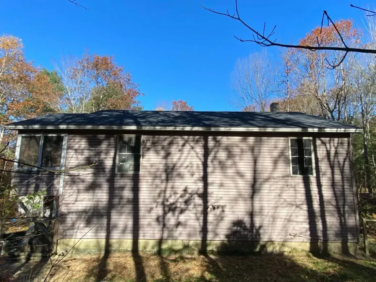A house with a roof that is surrounded by trees on a sunny day.