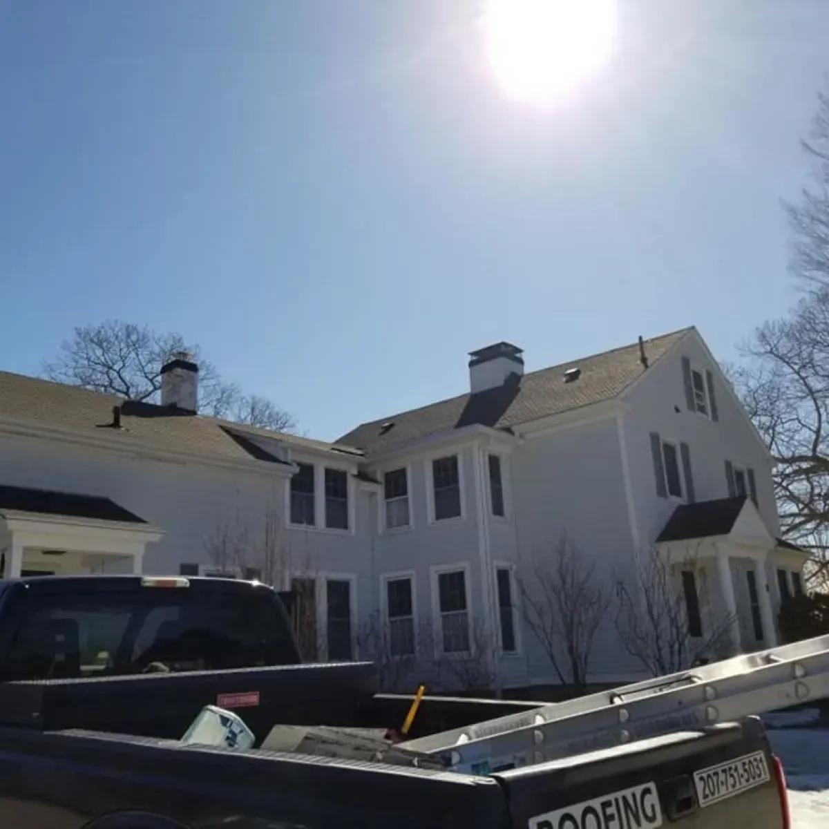 A roofing truck is parked in front of a white house