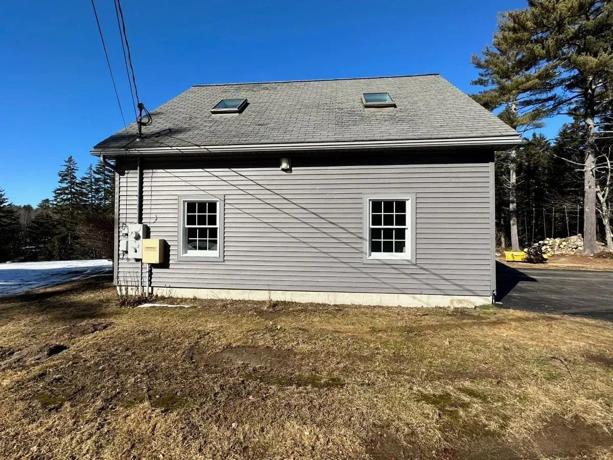 A small gray house with a skylight on the roof is sitting in the middle of a grassy field.