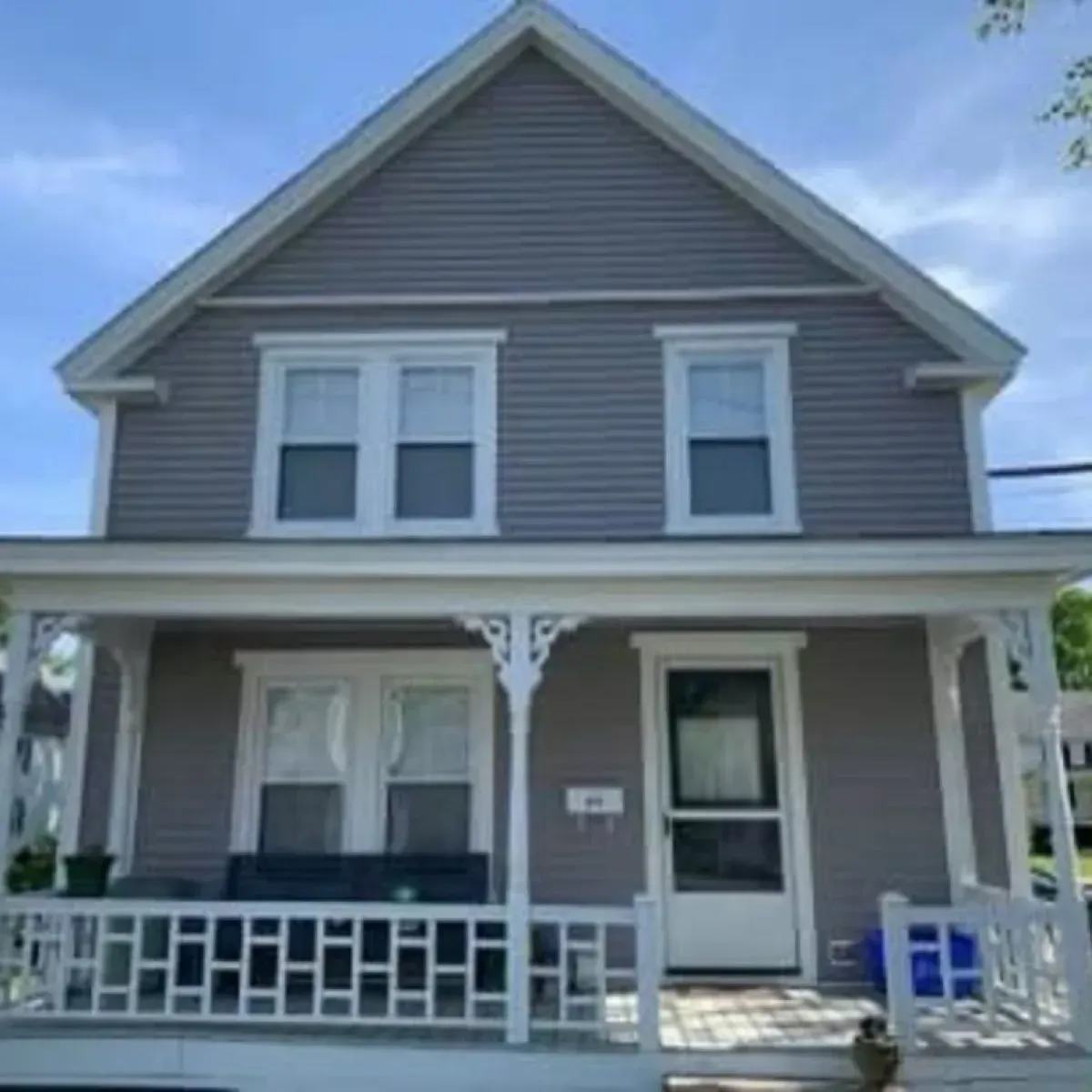 A gray house with a white porch and a blue sky in the background