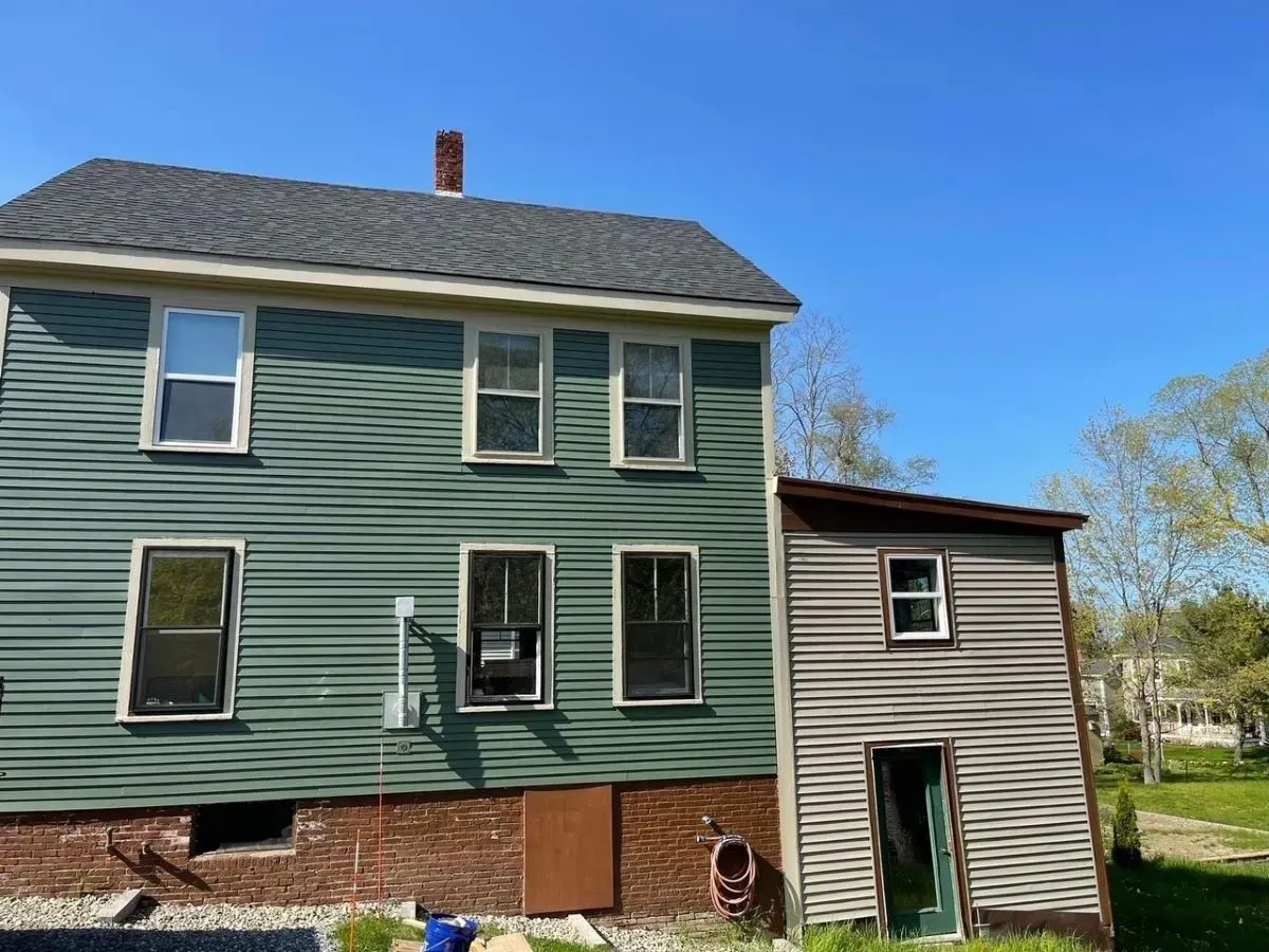 A green house with a black roof is sitting in the middle of a grassy field.