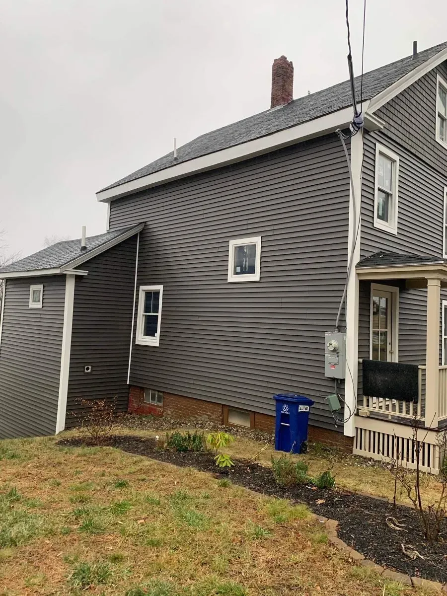 A large gray house is sitting on top of a grassy hill.
