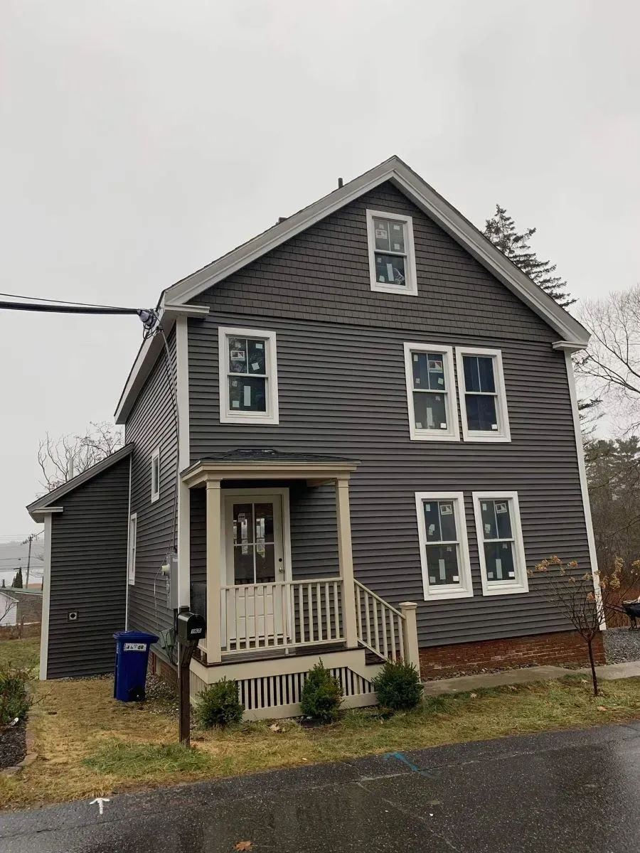 A gray house with white windows and a porch on a cloudy day.