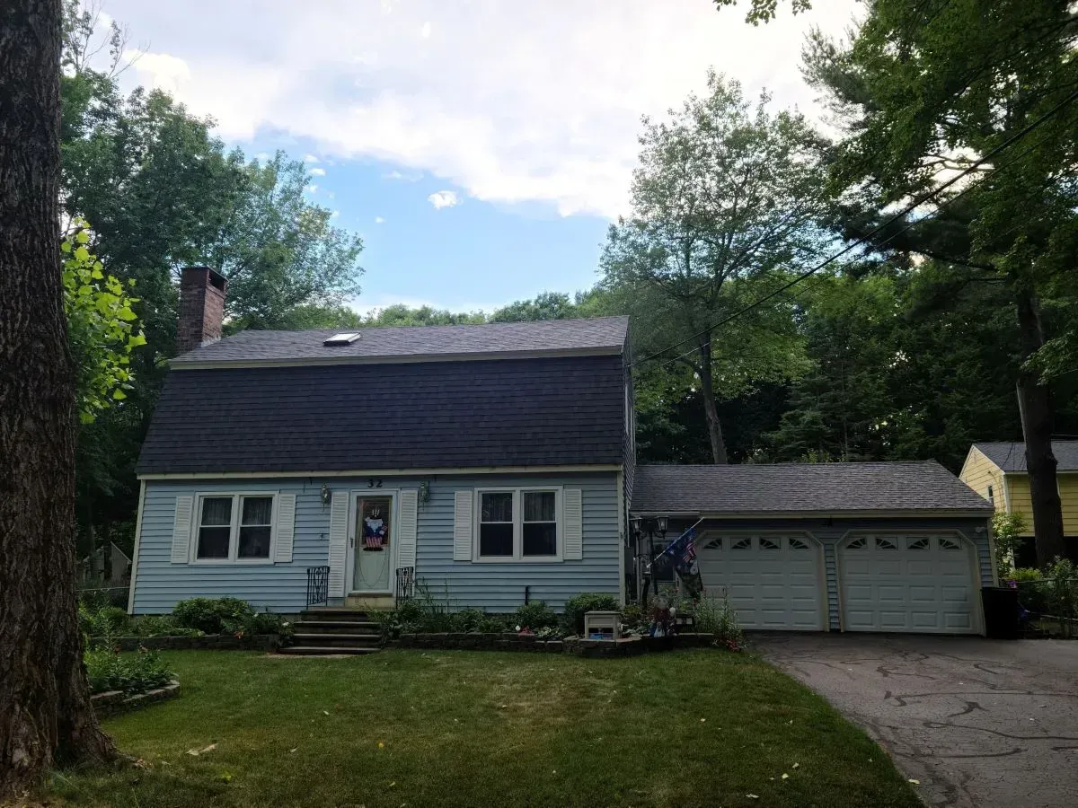 A blue house with a black roof and white shutters is surrounded by trees.