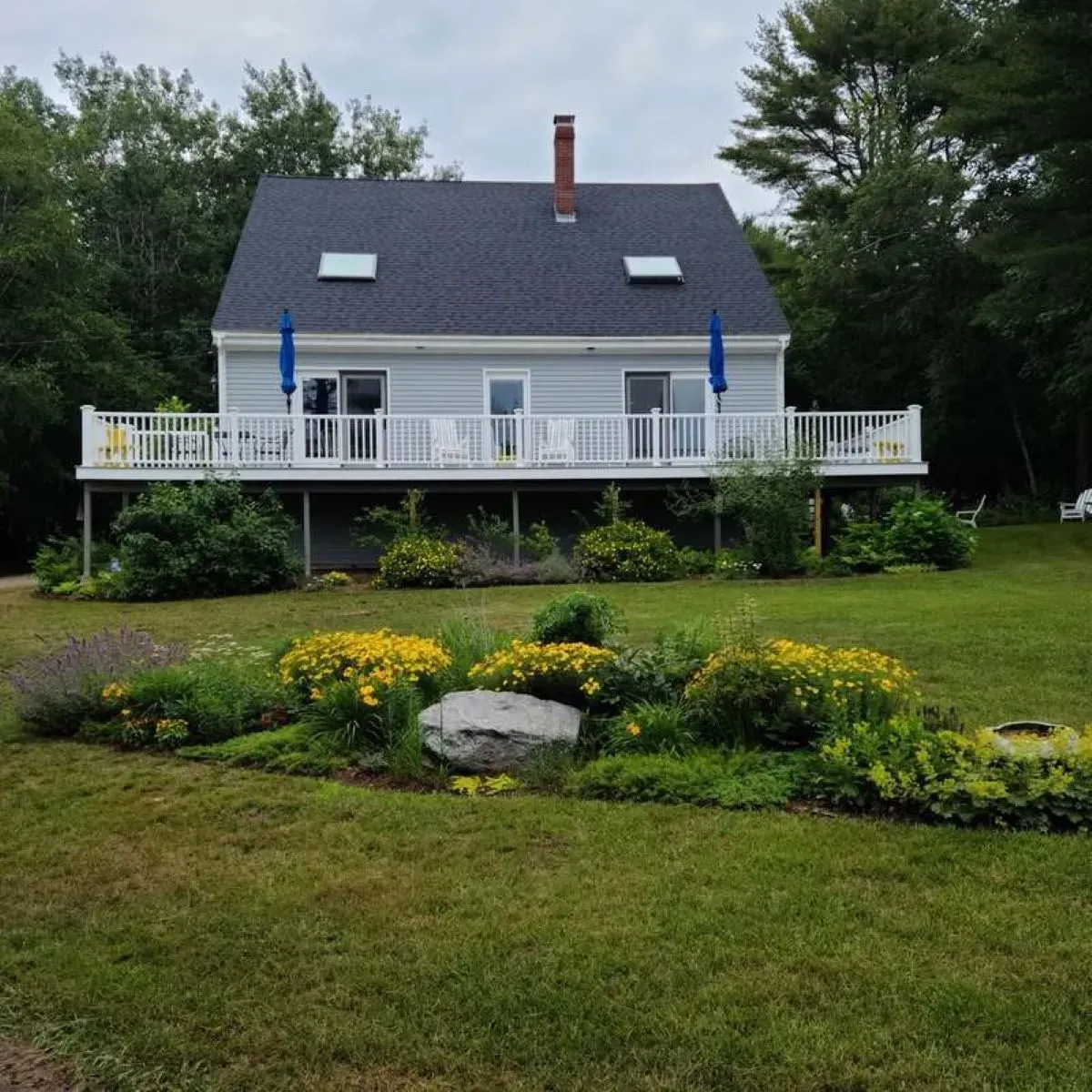 A white house with a large deck in the middle of a lush green field.