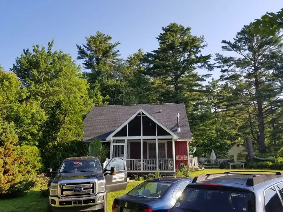 Two cars are parked in front of a house with a screened in porch