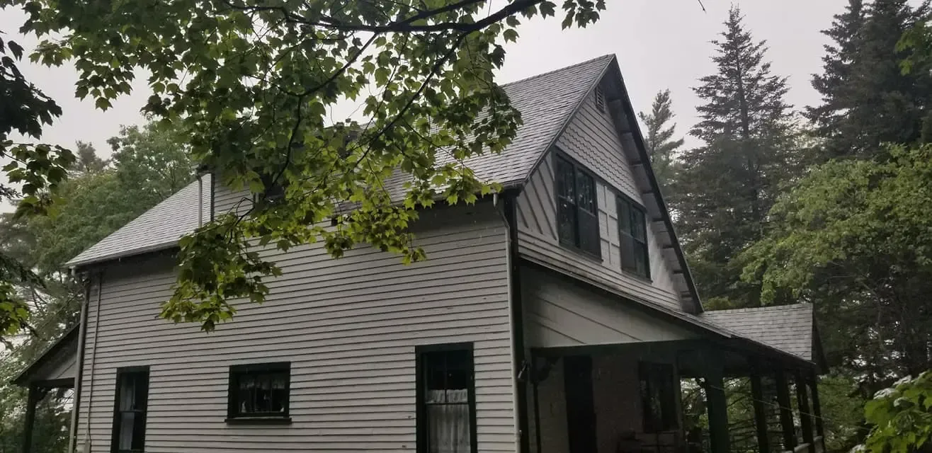 A white house with a porch is surrounded by trees on a cloudy day.