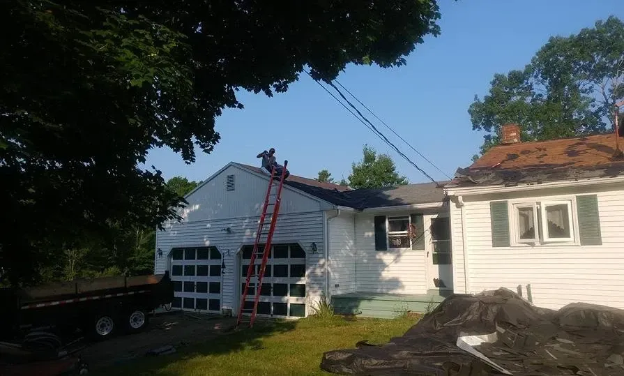 A man on a ladder is working on the roof of a house.