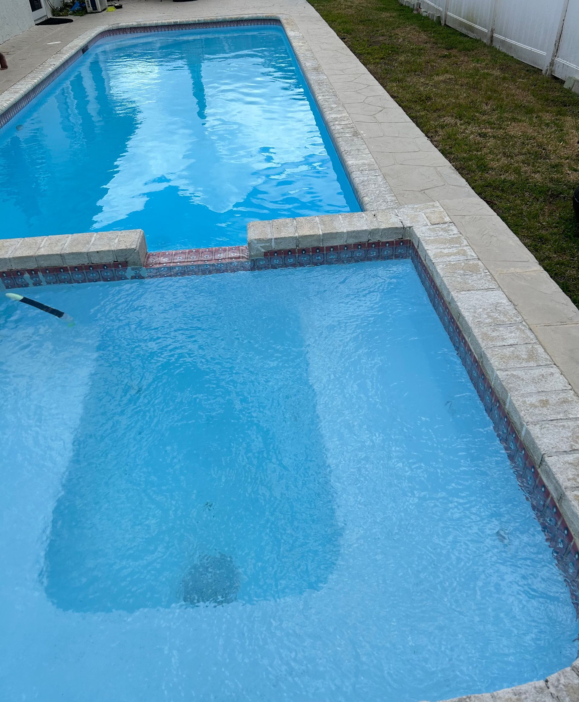 A view of a swimming pool through a window with blinds.