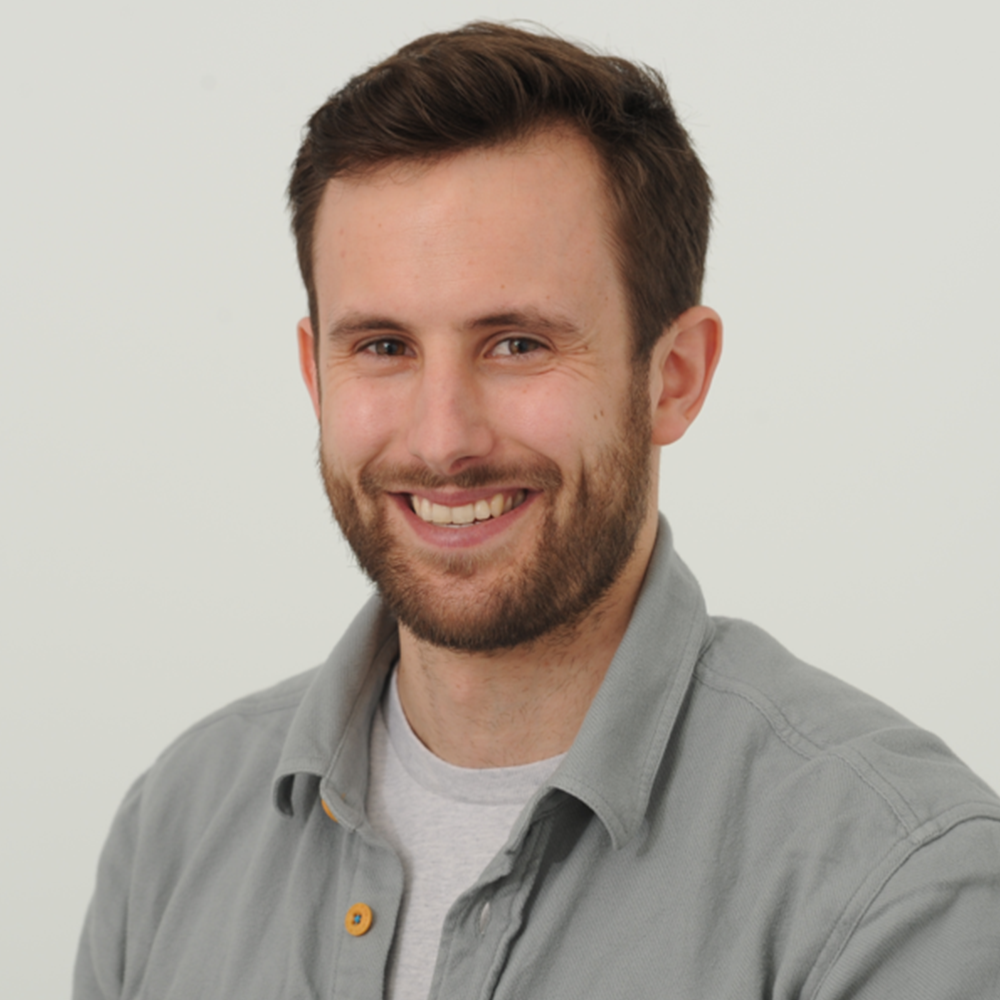 A man with a beard is smiling and wearing a grey shirt