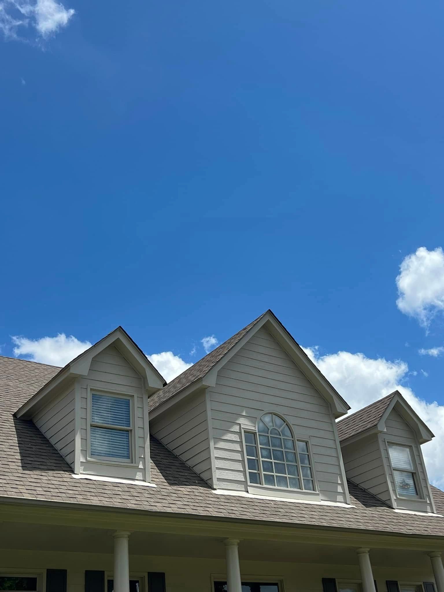 Gray house roof with dormer windows against a blue sky with small white clouds