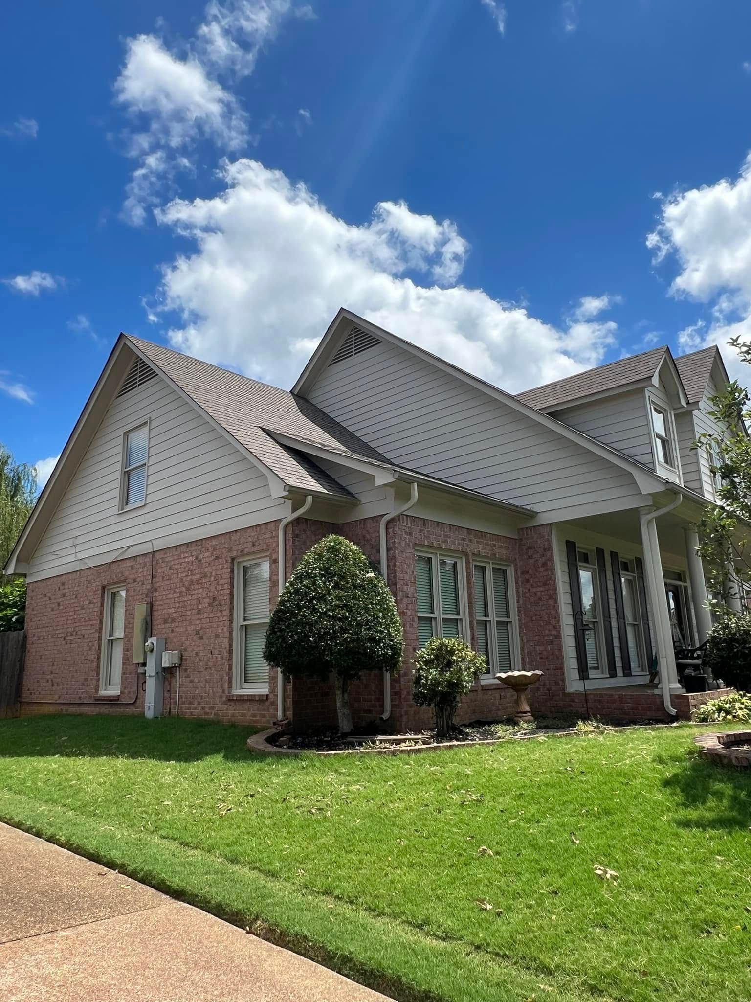 Brick suburban house with white trim, green lawn, and blue sky with clouds