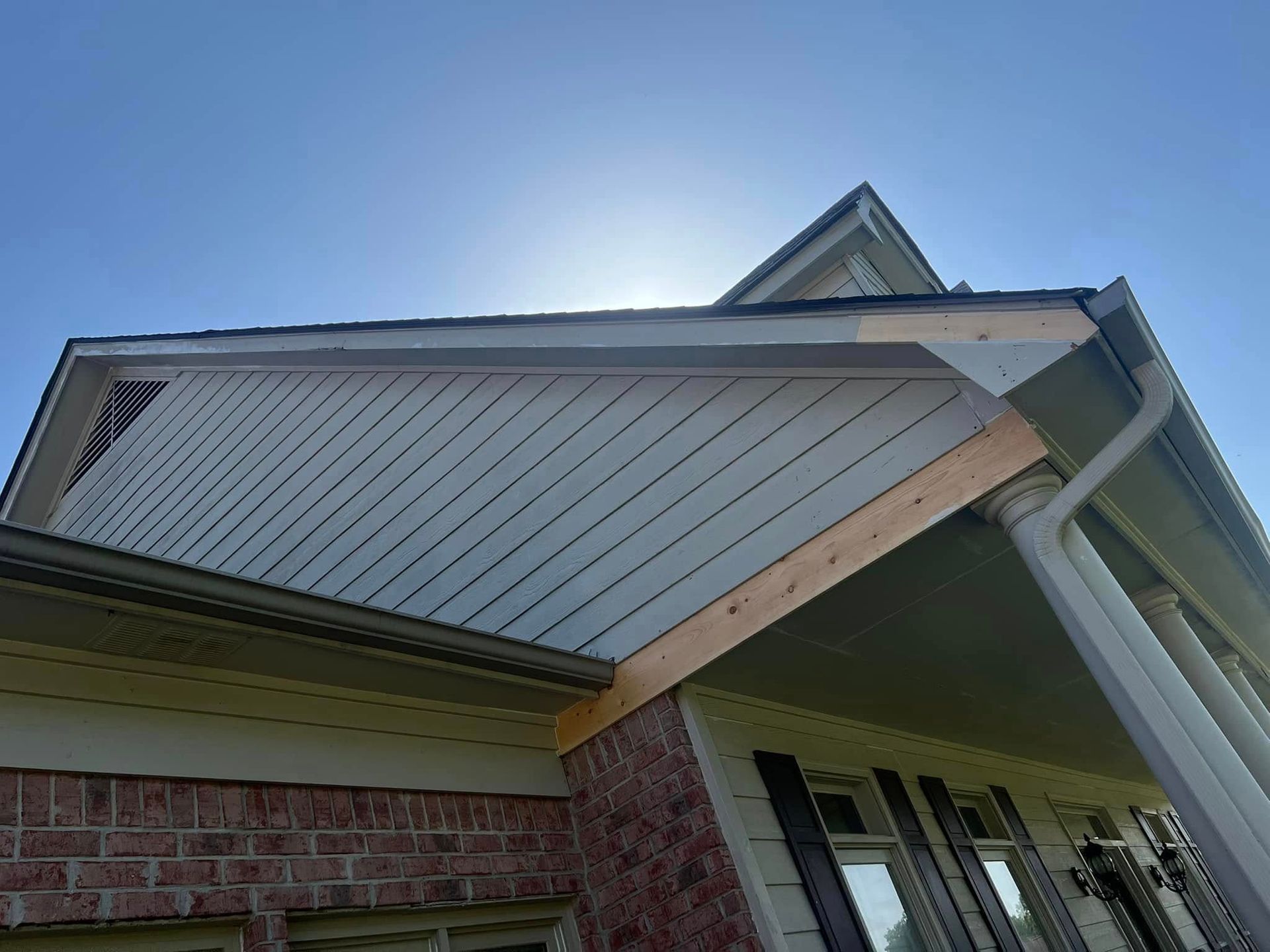 House exterior with brick siding, beige gable trim, and a white column against a blue sky