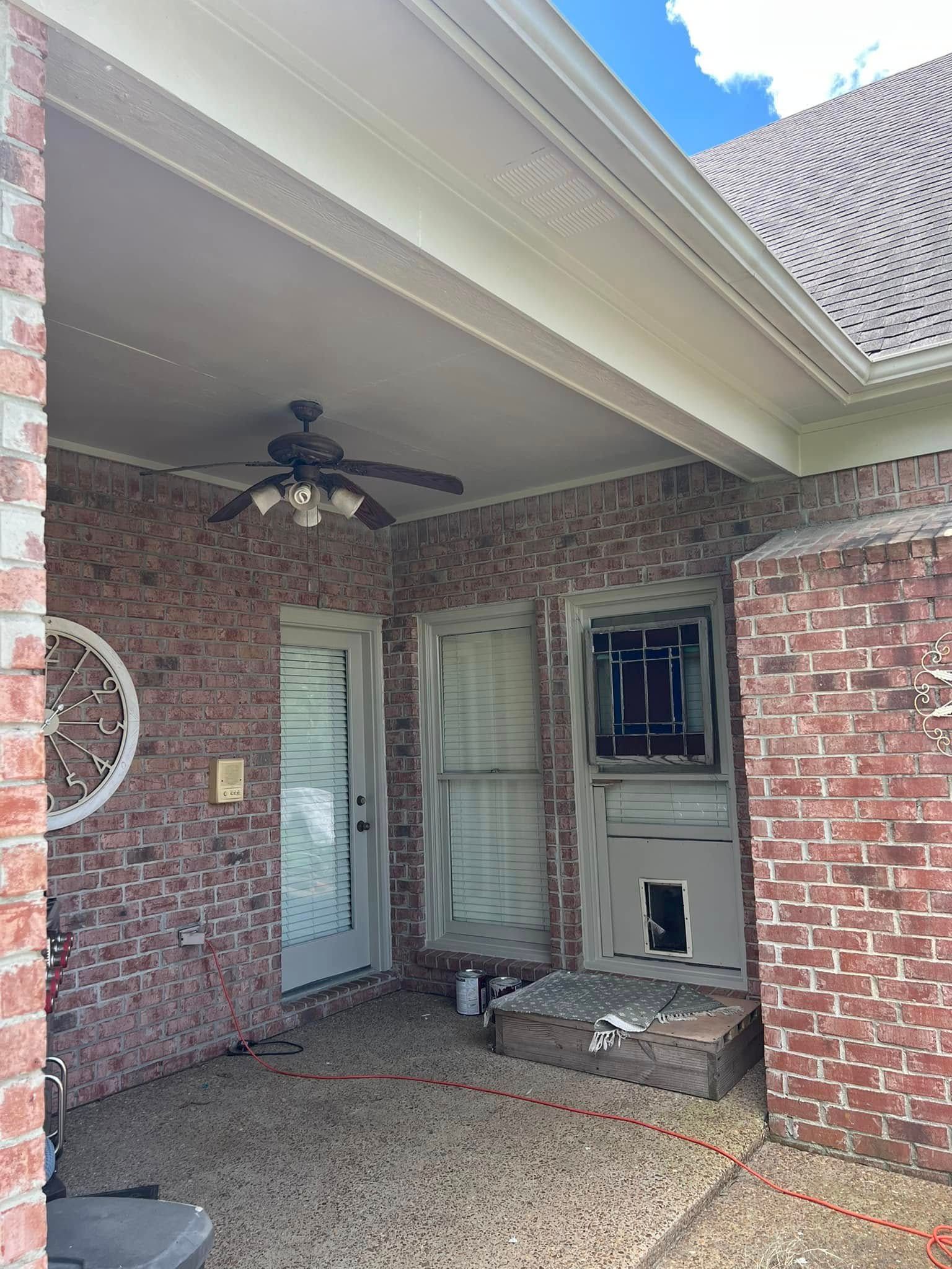 Brick-covered patio with ceiling fan, glass door, windows, and a small bench.
