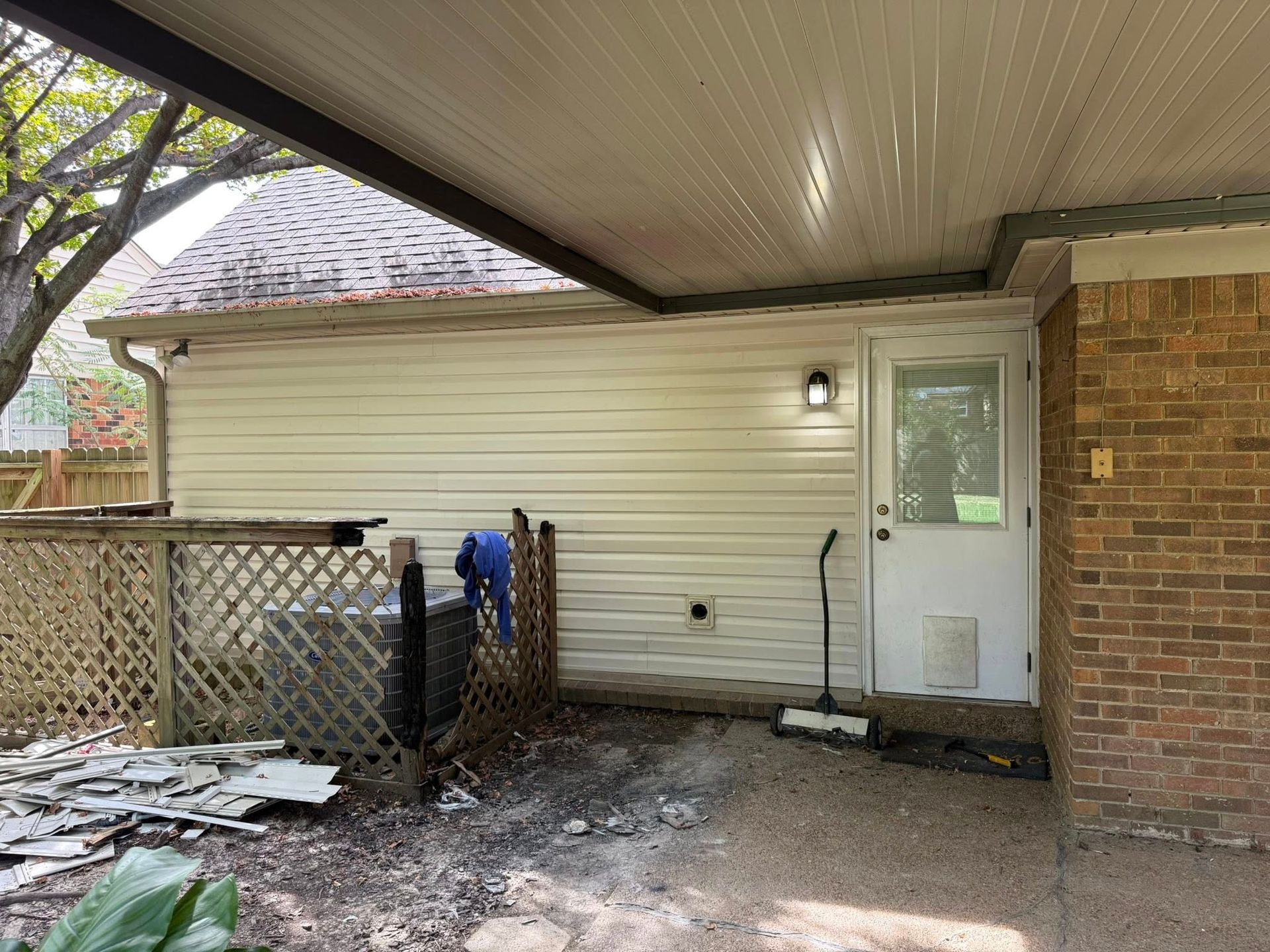 Side yard with white siding, brick wall, lattice fence, and two standing poles under a covered porch.