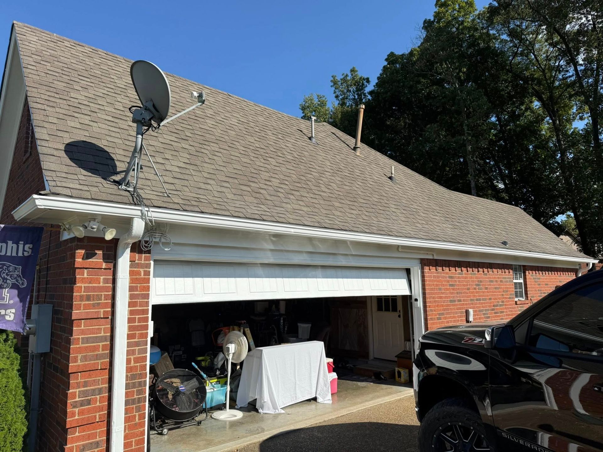 Brick house garage with open door, satellite dish on roof, and items stored inside on a sunny day