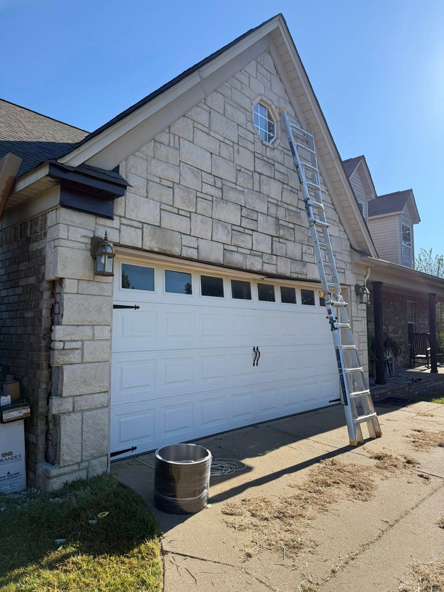 Stone house front with a white garage door and covered porch under a blue sky.