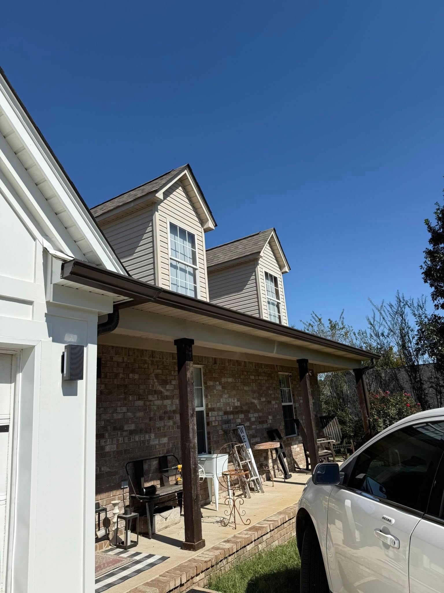 Brick house exterior with porch, white-trimmed gables, and parked SUV under a clear blue sky