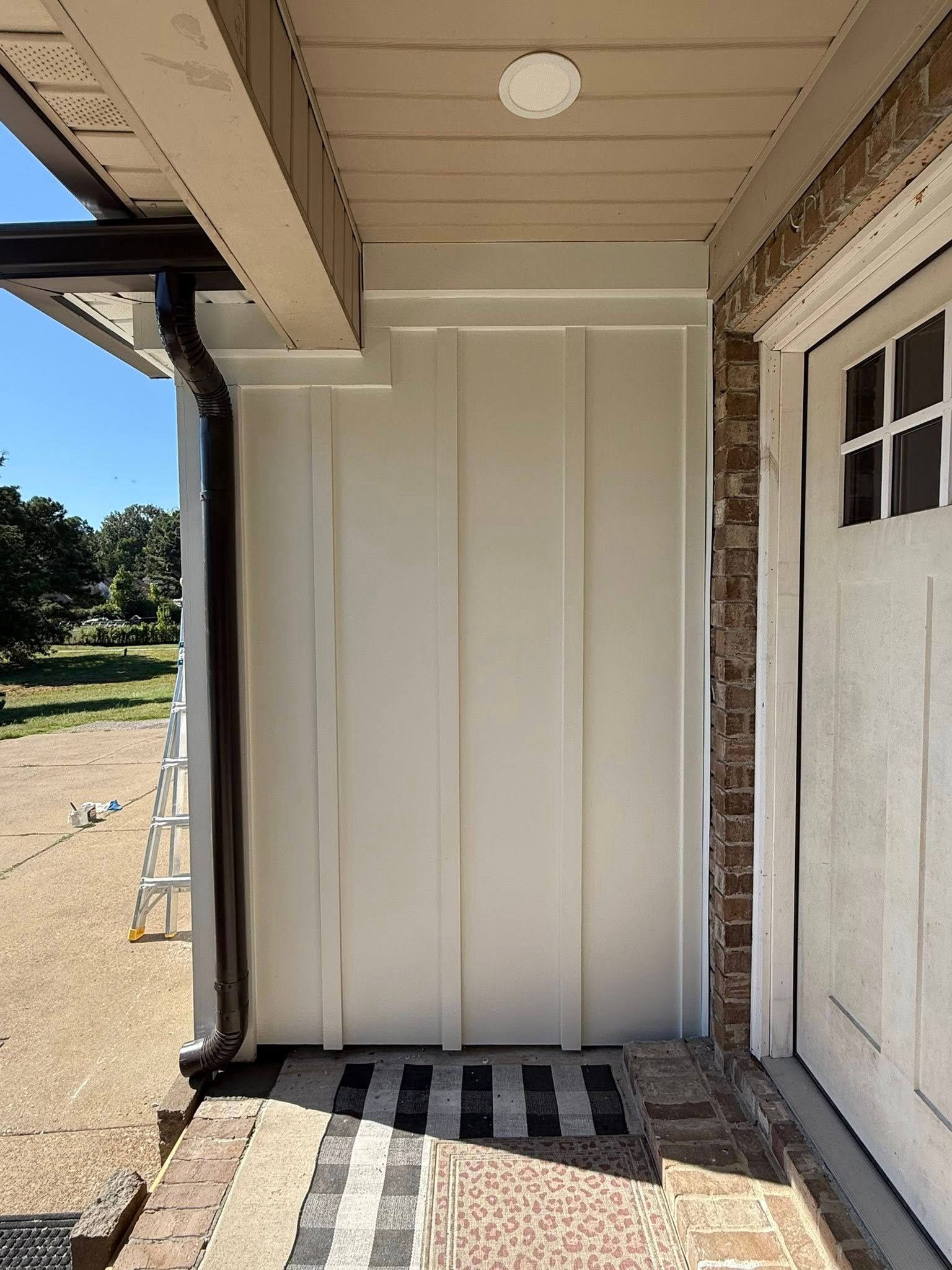 Front porch with white paneled door, brick wall, and striped doormat beside a second door.