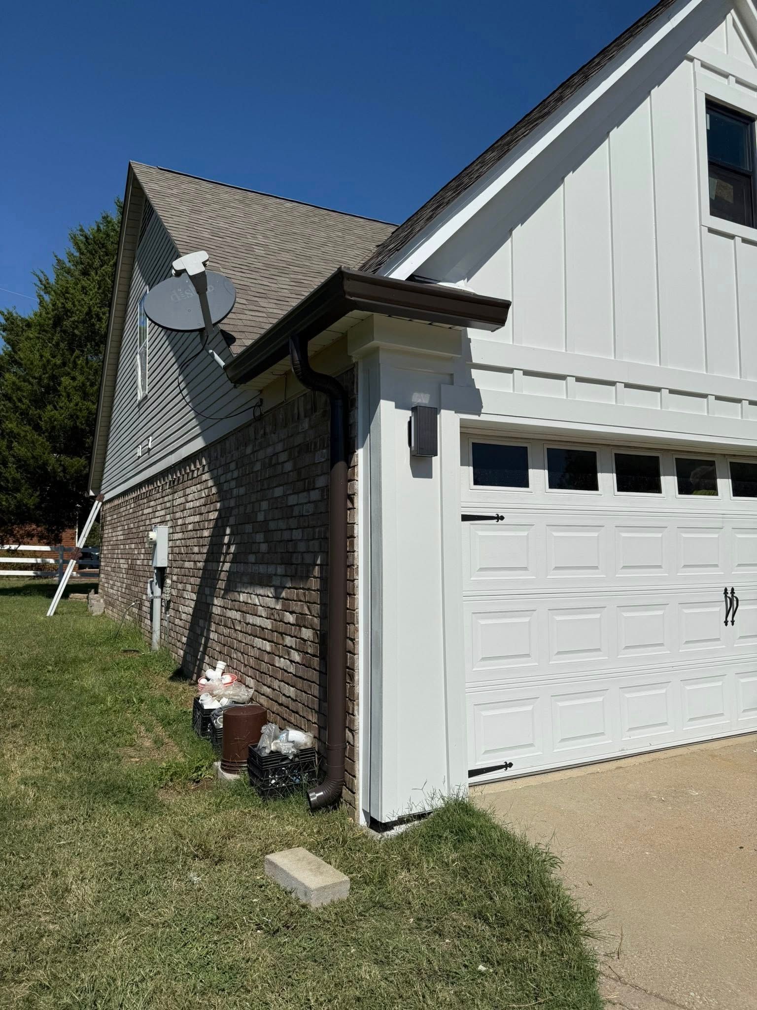 Side view of a house with white garage door, stone exterior, and satellite dish on a grassy lawn